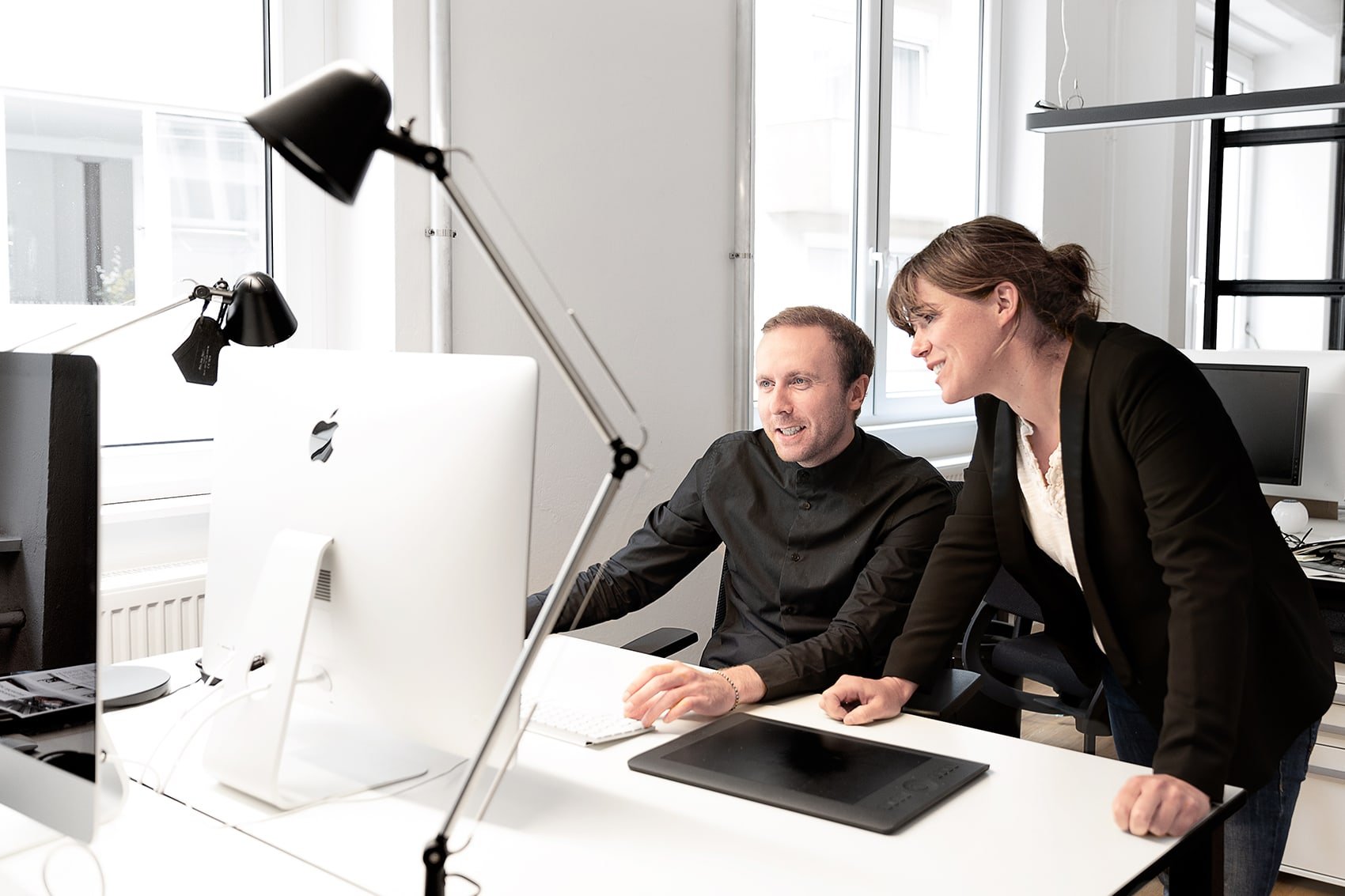 Zwei Kollegen arbeiten lächelnd am Computer in einem modernen Büro.