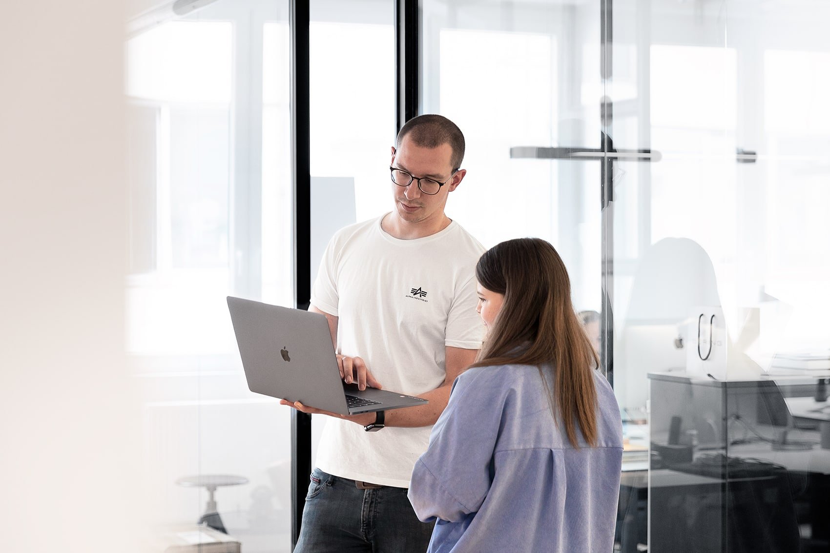 Zwei Personen in einem modernen Büro, die gemeinsam an einem Laptop arbeiten.