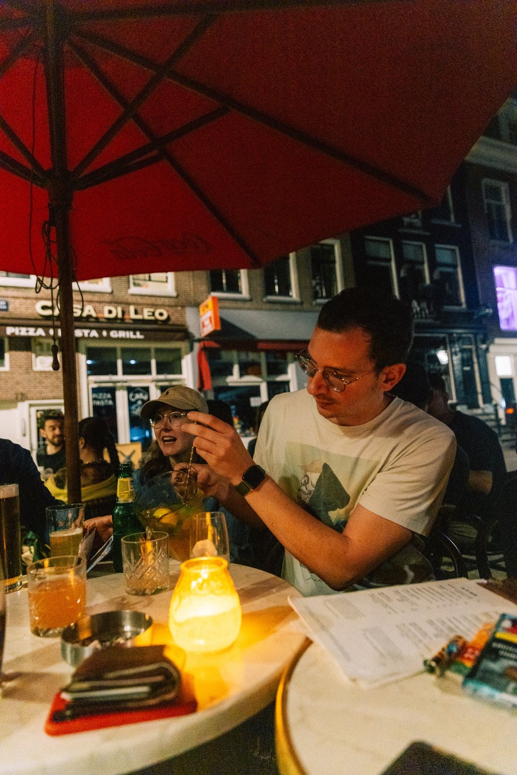 Gruppe von Menschen genießt nachts Drinks an runden Bistrottischen auf den Straßen von Amsterdam.
